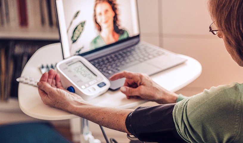 A woman is testing her blood pressure on a device while on a video call with her doctor.