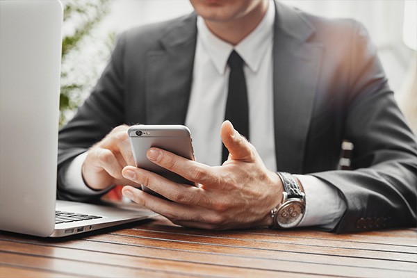 Business man holding mobile smart phone in front of laptop