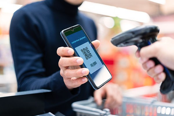 Person holding phone with QR code on screen being scanned in a retail setting