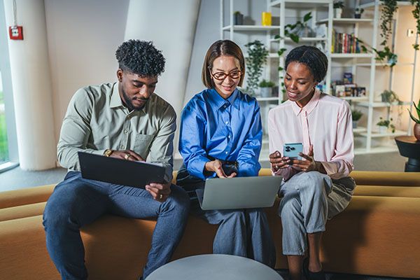 Diverse business colleagues working together on a laptop, tablet, and smart phone, smiling and discussing ideas during an informal meeting in a contemporary co-working office space