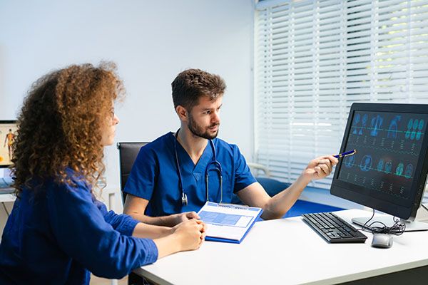 Male doctor explains health scan results to female patient using a computer screen. Concept of diagnosis, health tech, medical consultation, and digital healthcare.