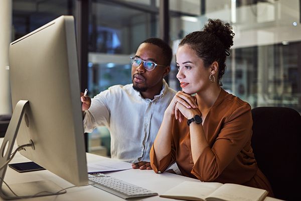 Business training, night planning and employees talking about corporate proposal on internet in dark office at night. African workers working on partnership on the web with computer during overtime.
