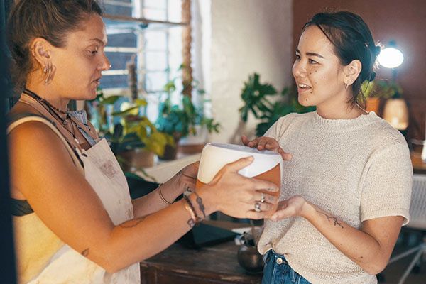 Customer service, shopping and women with pottery for assistance, help or show product. People, ceramics store and owner with client for sale, smile or giving pot for retail advice in small business.