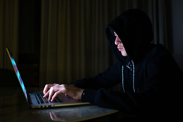 Hacker is  hacking into the computer network. Young boy in a dark room with laptop.  Hacker with a laptop.  Computer criminal. 