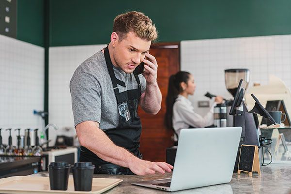 Cafe Owner barista receives order from customer on smartphone while using computer at coffee. Small business concept
