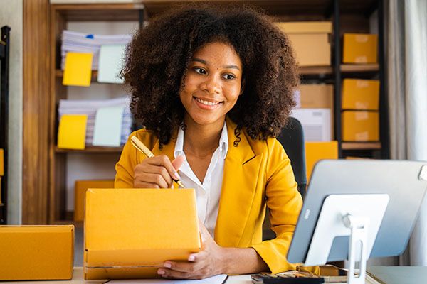 African American business woman working at warehouse preparing SME package box for delivery at small business home office.