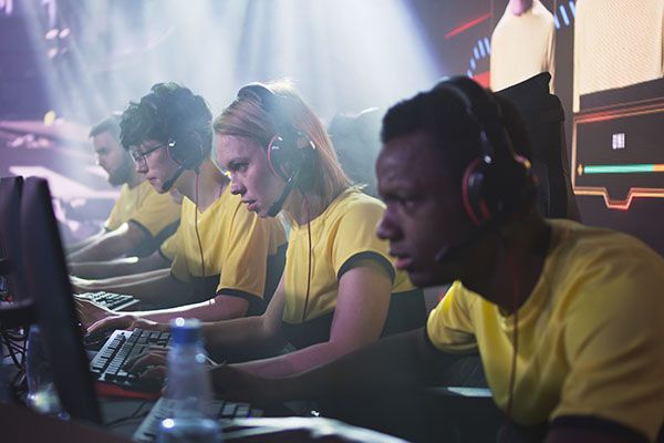 Concentrated blond woman esportsman gamer in headset playing video game on computer with multiracial teammates during professional esports competition