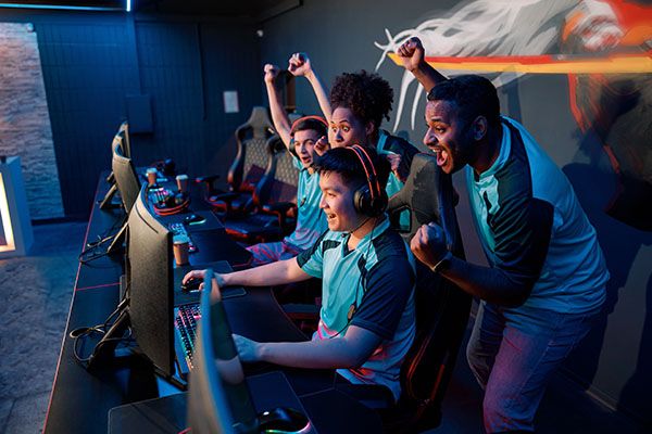 Multiracial team of happy professional cyber sports gamers celebrating success wile raising hands up during esports tournament in gaming club