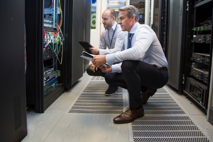 Computer technicians holding digital tablet while analysing server machines in server room.