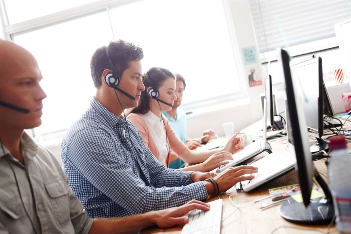 Sales assistants at the office working in front of their computers wearing headsets