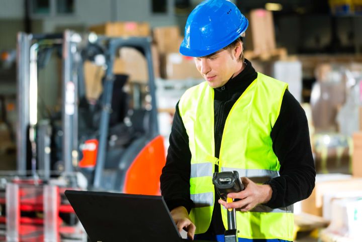 Warehouseman with protective vest, scanner and laptop in warehouse at freight forwarding company