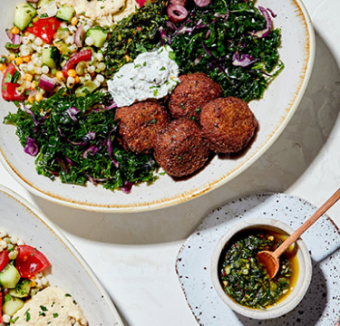 Delicious Mediterranean food (Falafel, Tabouli, Hummus, etc..) in serving plates on a table.