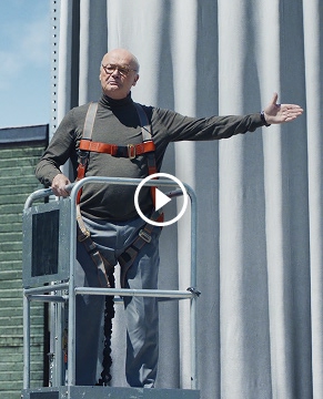 Creed stands on elevating bucket in the parking lot in front of Wake Up with Craig office, announcing something as Craig, Oscar, and Angela look on.